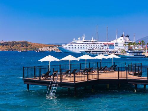 a dock with chairs and umbrellas and a cruise ship at Labranda TMT Bodrum in Bodrum City