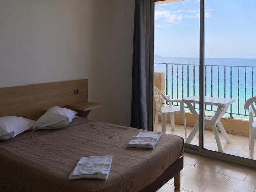 a bedroom with a bed and a balcony with a view at Hôtel A RENA D'ORU in Coggia