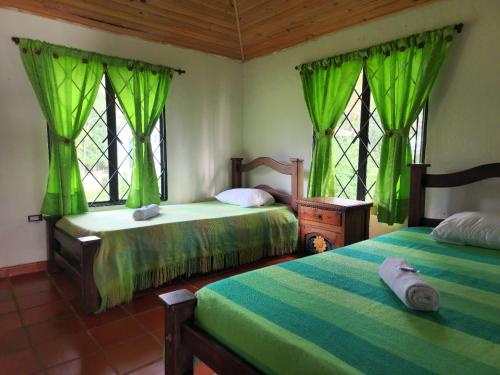 2 Betten in einem Zimmer mit grünen Vorhängen und Fenstern in der Unterkunft Hostel Lodge la Herradura in San José del Guaviare