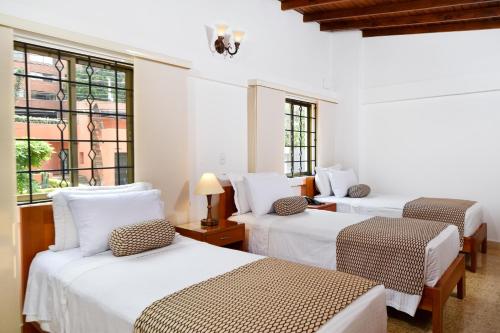 3 Betten in einem Zimmer mit weißen Wänden und Fenstern in der Unterkunft La Campana Hotel Boutique in Medellín