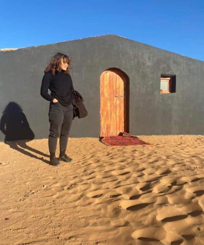 a woman standing in front of a building with a door at Mhamid Tours in Mhamid