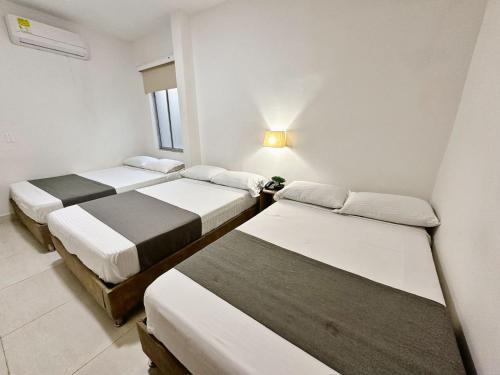 3 camas en una habitación con paredes blancas en Hotel Boutique Gao, en Cúcuta