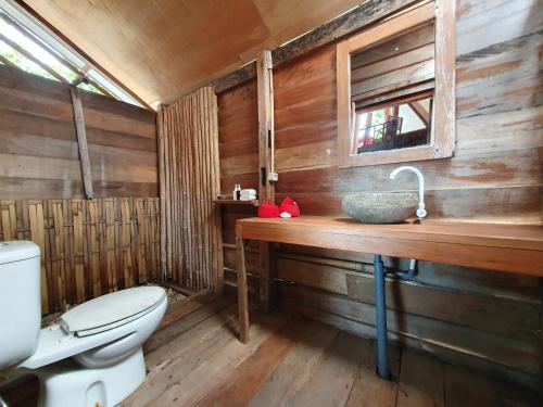 a wooden bathroom with a toilet and a sink at Sunset Moyo Bungalows in Moyo Island