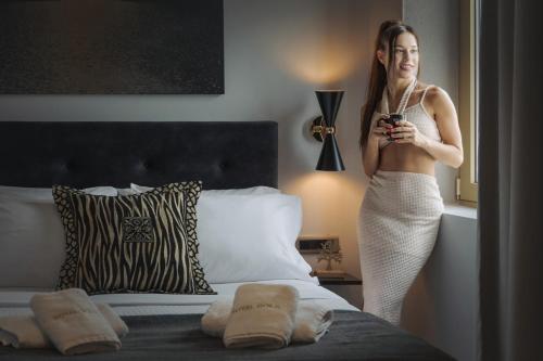una mujer de pie junto a una cama con un celular en Royal Gold City Suites by Estia, en Heraclión