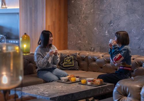 Zwei Mädchen sitzen mit Getränken auf einem Sofa. in der Unterkunft The Millennials Kyoto in Kyoto