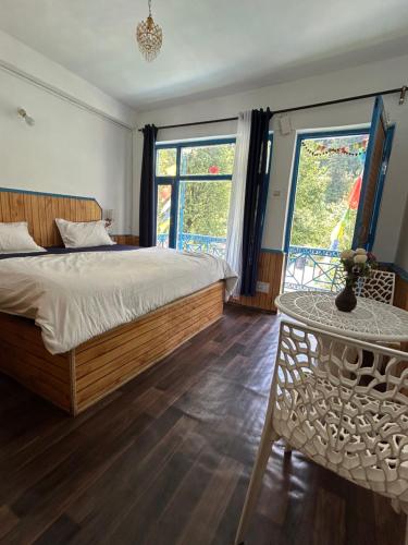 een slaapkamer met een bed en een tafel en ramen bij Tiny Spot Hostel in Manāli