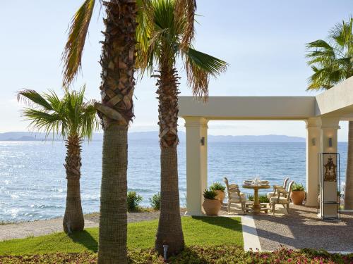 a house with palm trees in front of the ocean at Mandola Rosa at Riviera Olympia, A Grecotel Resort to Live in Loutra Killinis