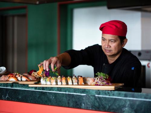 a man in a red hat preparing food on a table at Mandola Rosa at Riviera Olympia, A Grecotel Resort to Live in Loutra Killinis