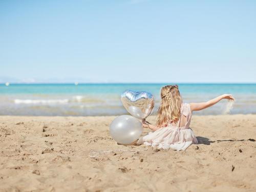 a little girl sitting on the beach with balloons at Mandola Rosa at Riviera Olympia, A Grecotel Resort to Live in Loutra Killinis