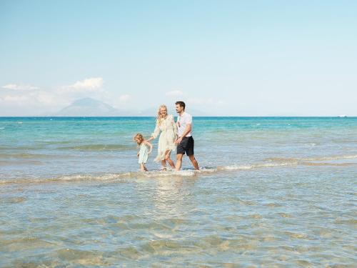 a family walking in the water on the beach at Mandola Rosa at Riviera Olympia, A Grecotel Resort to Live in Loutra Killinis