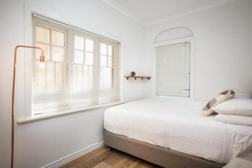 een witte slaapkamer met een bed en een raam bij Suburban Two-bed Apartment with Parking and Patio in Sydney