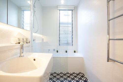 a white bathroom with a sink and a tub at Spacious 3-Bed Family House with Courtyard in Sydney