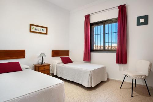 a bedroom with two beds and a window with red curtains at Casa Buganvilla in Conil de la Frontera