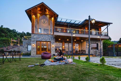 two people sitting on a blanket in front of a house at SaffronStays Aruunoday - 4BR with Theatre, Deck & Bonfire in Bhīm Tāl