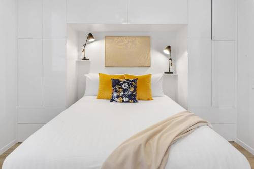 a white bedroom with a large white bed with yellow pillows at Spacious 2-Bed Unit With Balcony Next to The Gabba in Brisbane
