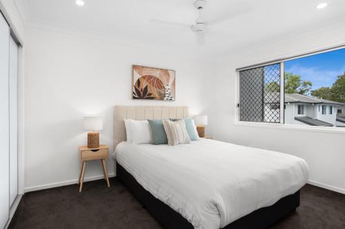 a white bedroom with a large bed and a window at Charming 3-Bed House with Patio near Sport Stadium in Brisbane