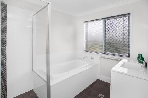 a white bathroom with a tub and a sink at Charming 3-Bed House with Patio near Sport Stadium in Brisbane