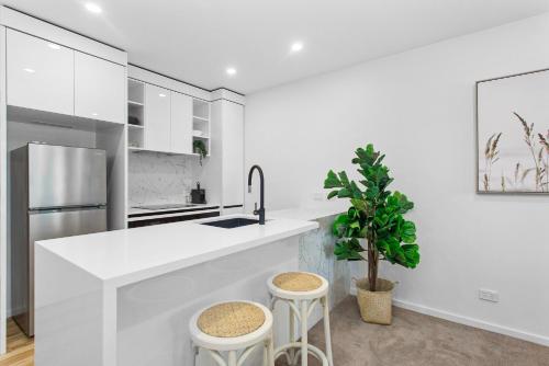a white kitchen with a sink and stools at Central 2-Bed with Gym, BBQ & Stunning Views in Canberra