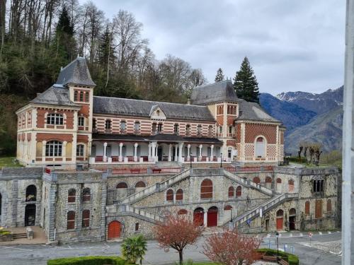 een groot bakstenen gebouw met bergen op de achtergrond bij Ô Cocon Montagnard in Eaux-Bonnes