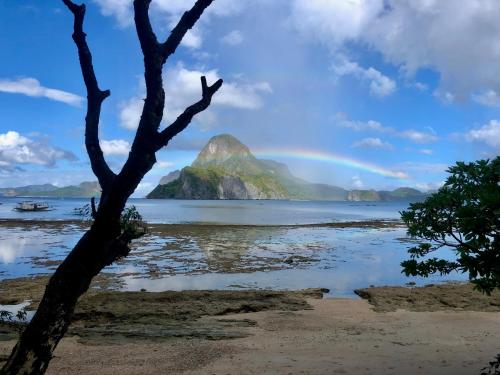 a rainbow over a mountain in the ocean with a tree at OIA Beach Hostel - El Nido in El Nido