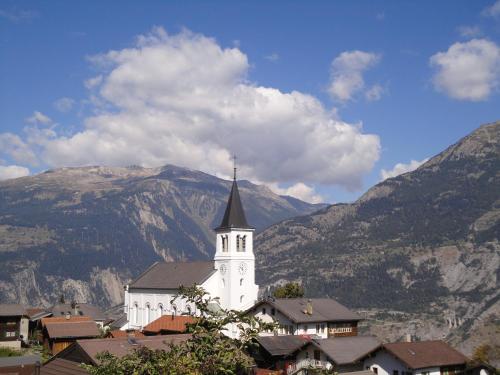 a white church with a steeple with mountains in the background at B&B Eischoll in Eischoll