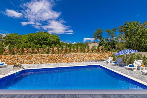 a swimming pool with chairs and a stone wall at Vila KATHARINA s privatnim bazenom in Žgaljić