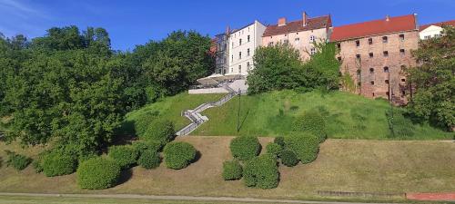 a building on top of a green hill with trees at City Center Apartment 45m, 1 Bedroom and 1 Living Room with Kitchen plus Bathroom, a perfect Family Friendly Place or for Home Office and a longer Stay, a proper office desk with business chair provided, 100m from Market Square and Vistula River in Grudziądz