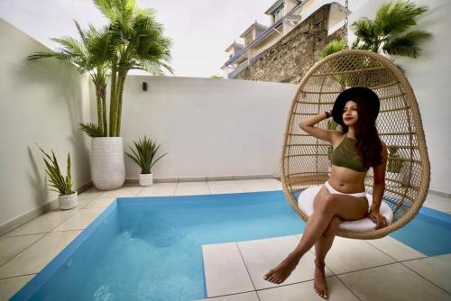 Maison Le Patio في سان دوني: امرأة جالسة على كرسي رتان بجوار حمام سباحة