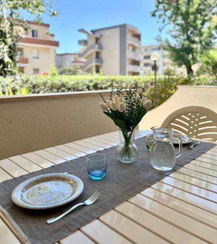 una mesa con un plato y un jarrón de flores en Nura's - Casa Flor Seaside, en Alghero