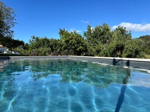 a swimming pool with blue water and trees in the background at Casa S.Cláudio - rural home near Viana do Castelo in Nogueira