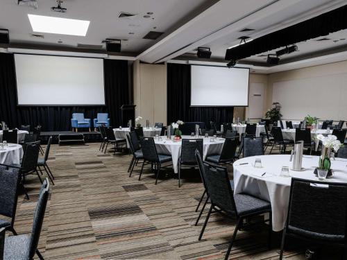um salão de banquetes com mesas e cadeiras brancas e ecrãs em ibis Sydney Olympic Park em Sidney