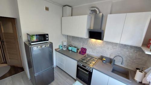 a kitchen with white cabinets and a stainless steel refrigerator at Słoneczne Mieszkanko Przymorze 2 km do plaży in Gdańsk