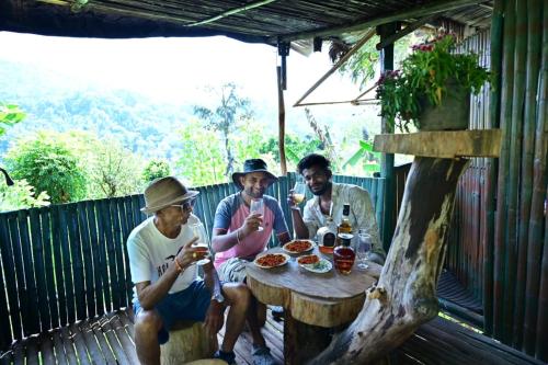 Eine Gruppe von drei Männern, die an einem Tisch sitzen und Essen essen. in der Unterkunft Harakoppa Hills in Padakalu