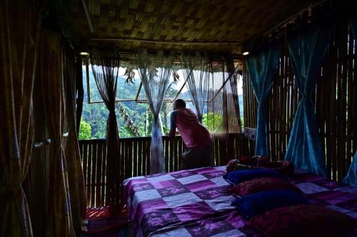 eine Person, die aus einem Fenster auf ein Bett blickt in der Unterkunft Harakoppa Hills in Padakalu