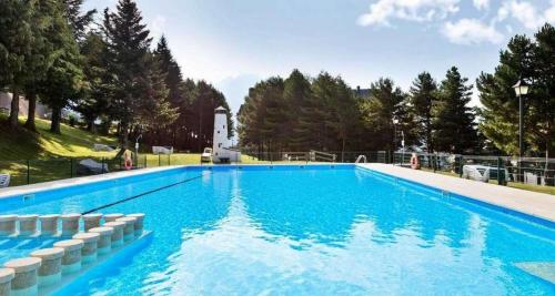a large blue swimming pool with trees in the background at Apartamentos Baladrias Formigal Centro - Recién Reformado in Formigal