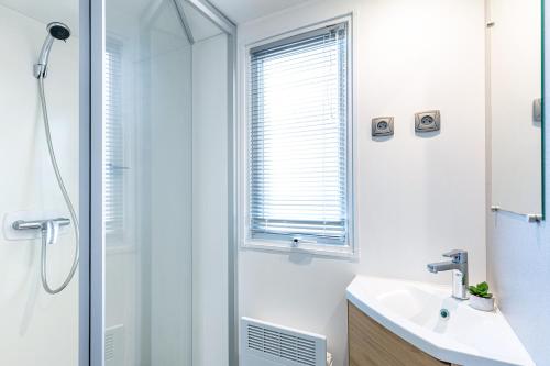 une salle de bain blanche avec une douche et un lavabo dans l'établissement Mobil home, piscine chauffée, toboggan, accès plage direct - 3 chambres 6 personnes, à La Turballe