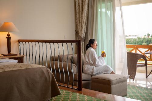 a woman in a robe sitting on a chair in a bedroom at Movenpick Taba Resort & Spa in Taba