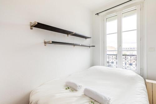 een witte slaapkamer met een bed en een raam bij GuestReady - Parisian Perch with Eiffel Tower View in Parijs