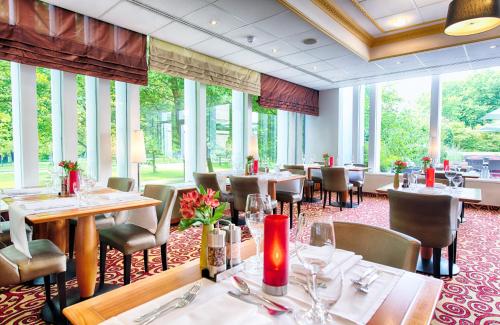 un restaurante con mesas, sillas y ventanas grandes en Leonardo Hotel Hamburg City Nord, en Hamburgo