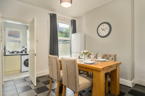 a dining room table with chairs and a clock on the wall at Willow House - 2-Bedroom House In Merseyside! in Birkenhead