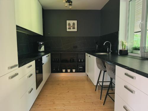 a kitchen with black walls and white cabinets and a wooden floor at Valmiera Riverside Retreat - Beverina Secret in Ķeiži