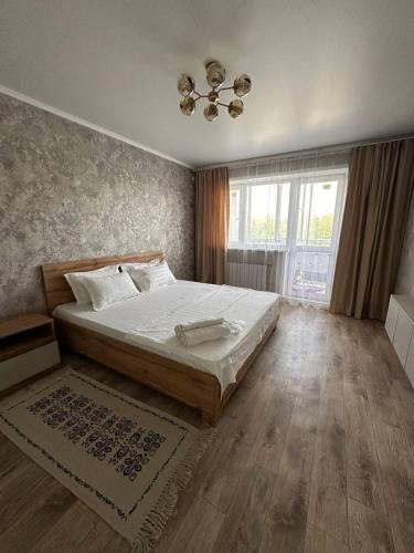 ein Schlafzimmer mit einem Bett und einem großen Fenster in der Unterkunft Уютная квартира недалеко от Аэропорта in Qostanai