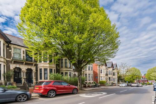 a red car parked next to a tree on a street at Ty Ayla Premier Apartments - Roath Park in Cardiff