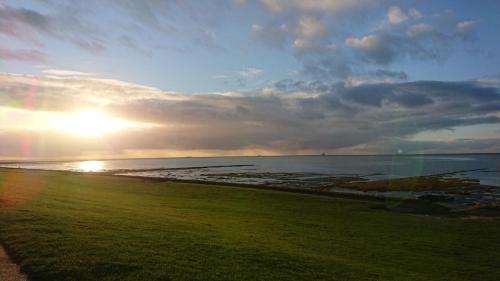 a view of the ocean with the sun setting on the beach at Ferienhaus Norderpiep 54 in Friedrichskoog