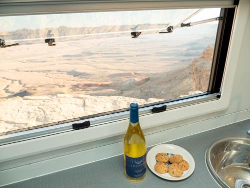 a bottle of wine and a plate of cookies in front of a window at קראוון מדברי במכתש רמון in Mitzpe Ramon