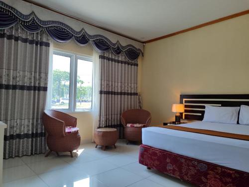 a bedroom with a bed and two chairs and a window at H.V HOTEL BANDARA in Gorontalo
