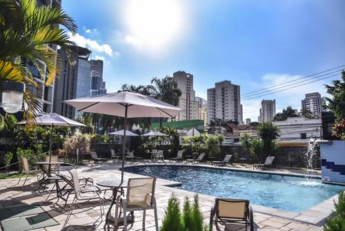 uma piscina com cadeiras e mesas e um guarda-sol em Plaza Inn Small Town Flat em São Paulo