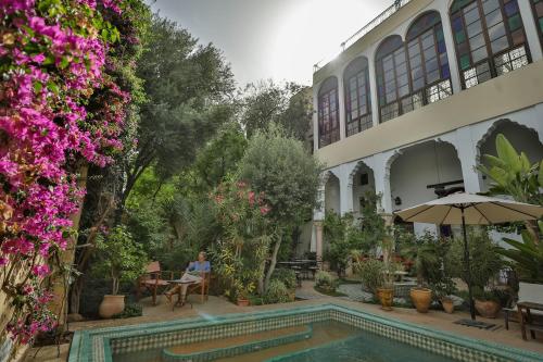 a woman sitting at a table next to a house with a swimming pool at Ryad Mabrouka in Fès