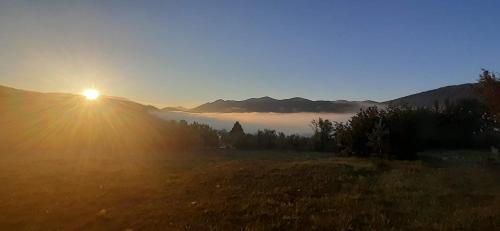 a sunset over a field with the sun rising over the mountains at Kuća za odmor Dangubica in Kuterevo