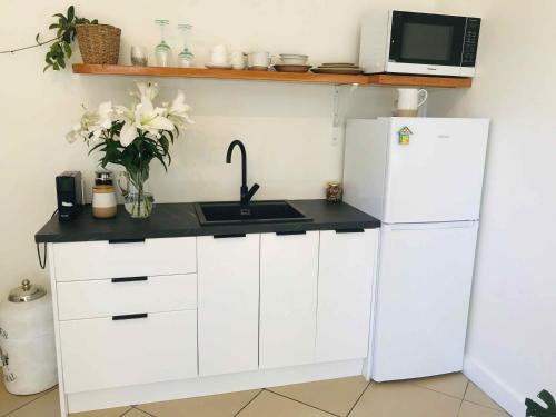 een witte keuken met een wastafel en een koelkast bij Serendipity Adorable Tairua Studio in Tairua